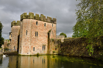Fototapeta na wymiar Sun on Bishop's Palace Gatehouse with bridge over the moat with swan and ducks under cloudy sky in Wells Somerset England