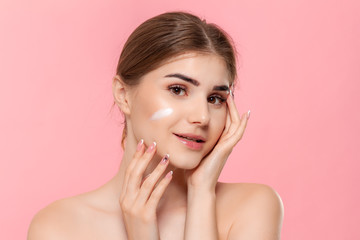 Obraz na płótnie Canvas Beautiful model applyes moisturizing cosmetic product to skin holding white tube of a hyaluronic cream isolated over pink background. Concept of beauty and health treatment.