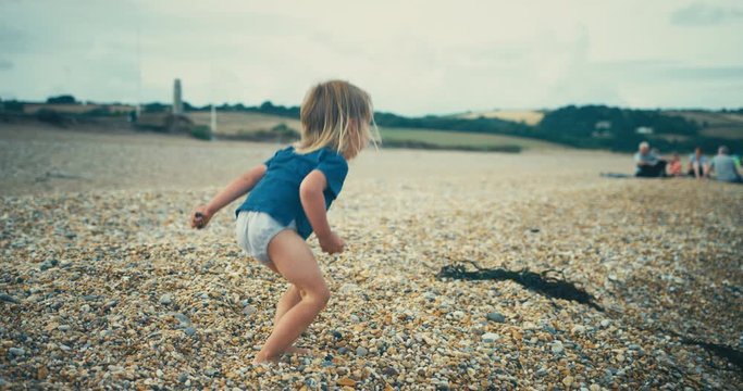 Little toddler boy walking on the beach and throwing stones