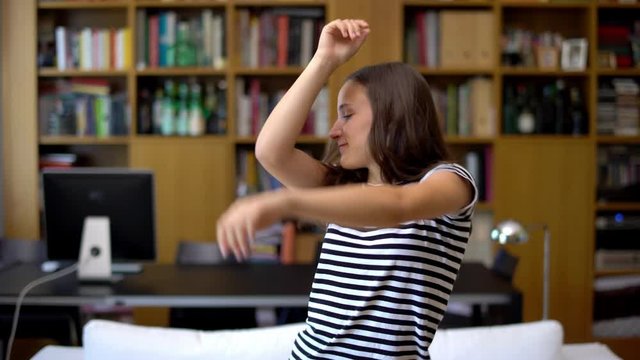 Pretty beautiful young woman dancing happily at home near a bookshelf. Modern student schooler teenager girl dancing in modern house living room, having fun enjoying.