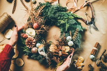 Top view Christmas wreath on craft background, pretty famales hands decorate christmas wreath.