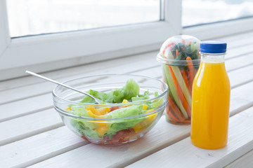 Bowl of green salad, raw vegetables and bottle of orange juice. Weight loss, diet and right...