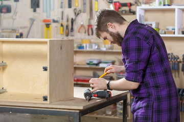 Young bearded man working at the furniture factory