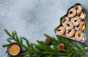 Christmas cookies in a box in the form of a Christmas tree. Green branches with pine cones. Hot chocolate in a metal mug. Flat Lay