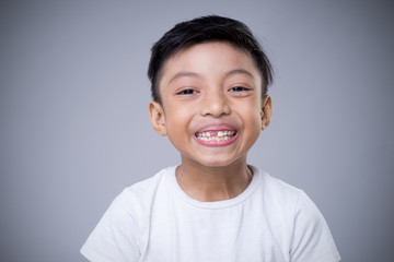An Asian boy smiling wearing a white t-shirt on a grey background. 