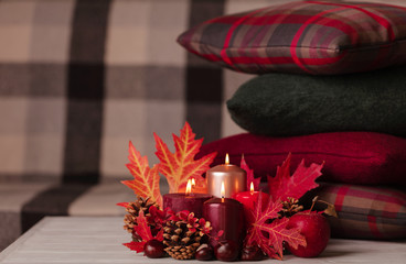 Autumn still life - candles, leaves and cones on the background of pillows.