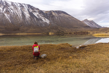 Fototapeta premium Rear view of young woman taking rest against snow-capped mountains and lake during winter season in Patagonia, Argentina