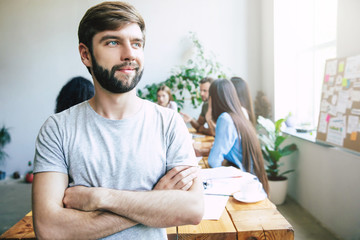 Handsome young business man in smart casual wear on background of brainstorming modern start up team in office or co-working centre