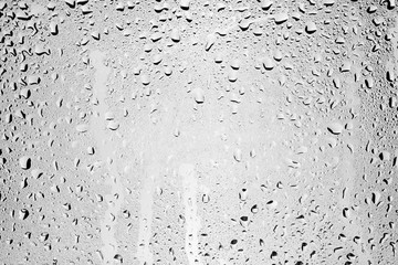 Drops of water flow down the surface of the clear glass on a gray background.