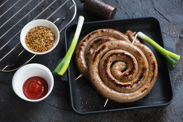 Cast-iron pan with fried coiled sausages, studio shot on a dark grey stone background