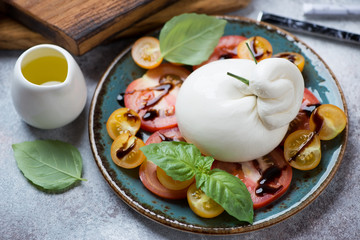 Burrata cheese and tomatoes salad served on a turquoise plate, studio shot on a beige stone surface