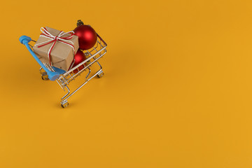 Gifts in a small shopping trolley on a yellow background, concept, copy space.