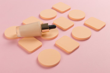 Sponges, a beautiful blender for applying foundation or powder and a bottle of concealer. Flat lay on a pink background, copy space.