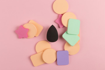 A lot of sponge, a beautiful blender for applying foundation or powder. Flat lay on a pink background, copy space.