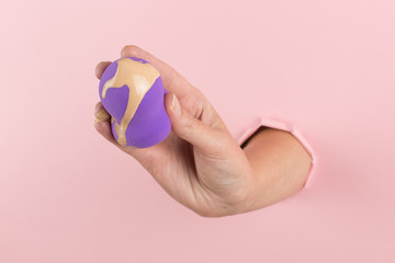 Girl hand holds a beauty blender in foundation, concealer from a hole in a pink background. Makeup artist concept, copy space.