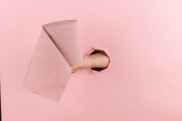 Woman hand holds toilet paper from a hole in a pink background. Concept, copy space.
