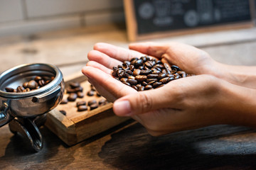 Beautiful hands holding coffee beans As a raw material for making coffee Refreshing drink Useful for the body with a glass coffee background and leaves from the coffee tree