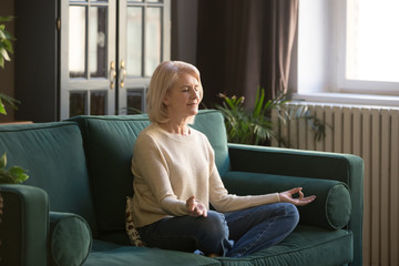 Obraz premium Calm senior woman meditating on couch at home
