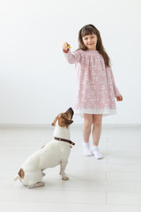 Positive little girl in a pink dress playing and feeding her little dog Jack Russell Terrier on a white background. The concept of favorite animals and dogs. Copyspace.