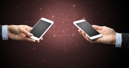 Close up of two hands holding smartphones to each other, wireless connection concept