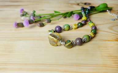 Beads from ceramics and natural stones and thistle flowers on a wooden table, composition with handmade jewelry.