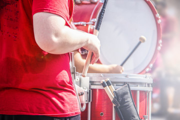 Closeup crop of girl in red tee shirt playing the drums in marching band with blurred drummer...