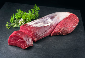 Rohes dry aged Rinderfilet Steak mit Bouquet Garni als closeup vor schwarzen Hintergrund mit...