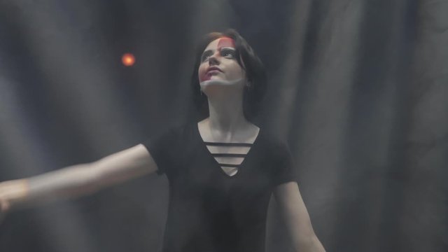 smiling young woman with haircut mimes extending hands to bright light rays in dark space slow motion