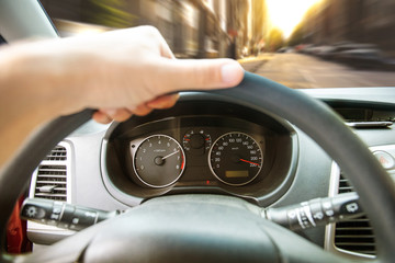 hand on the steering wheel of a fast racing car along a city street among houses, blurred road behind the windshield