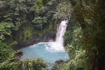 Beautiful waterfall of turquoise blue water, surrounded by green tropical vegetation.