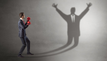 Businessman with boxing gloves fighting with disarmed businessman shadow