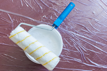 Paint roller and a can of white paint on the floor ,the floor is covered with a oilcloth for protection
