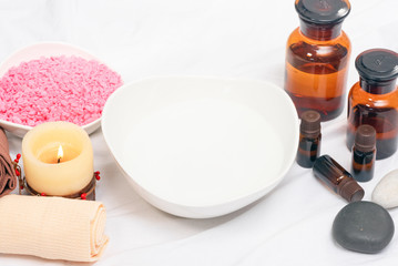 Aromatherapy oil bottles, burning candles, water in a bowl and towels on a wooden floor background.