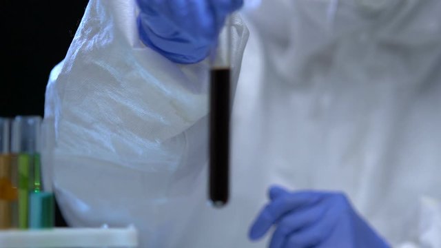 Chemist in protective uniform showing tube with dark liquid, oil examination