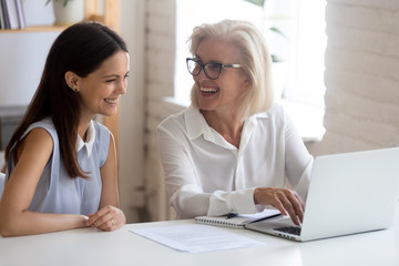 Happy female employees laugh discussing project at laptop