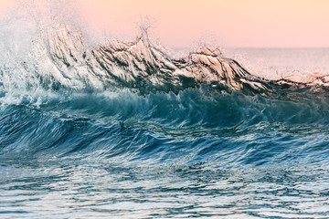 A close up of an ocean wave building up before crashing into the beach shore near the Pacific Coast Highway. During sunset, the background has high pink, purple, and red colors for a dramatic sunset.  - 288367631