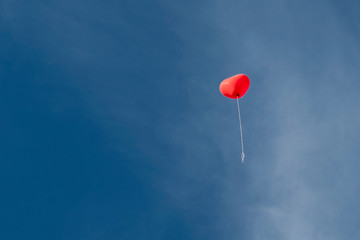 red heart shaped balloon in front of blue sky with clouds
