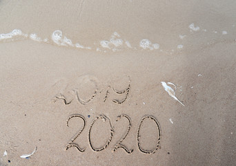 New Years 2020 replace 2019 concept. End of 2019 Happy New Year 2020, lettering on beach with wave and clear blue sea. Handwritten inscription 2019 and 2020 on beautiful sand beach.