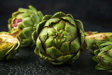 Fototapeta premium Fresh raw organically grown artichoke flower buds on dark background