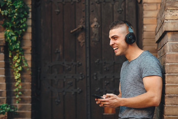 Fototapeta premium Young man listens to music through headphones and smiling in the city