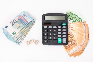 Taxes and spending concept. Tax word writen on wooden cubes. Euro banknotes Laid out in a semicicircle and calculator.Copy space for text. Euro money and calculator on white background.