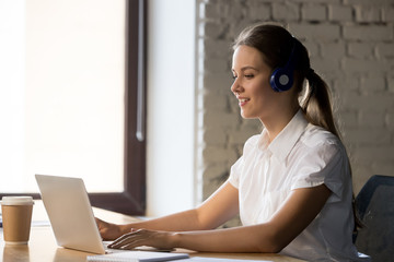 Smiling businesswoman wearing headphones using laptop at work