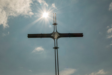 Summit cross with sun in front of blue sky