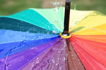 Krople deszczu spadające na parasol w kolorach tęczy, deszczowa pogoda.