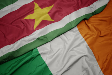 Obraz premium waving colorful flag of ireland and national flag of suriname.