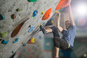 young active sport caucasian man with beard and glasses climbing on gym wall during bouldering workout - obrazy, fototapety, plakaty
