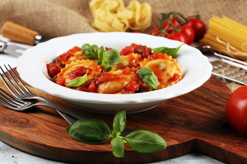 Ravioli with tomato sauce garnished with parmesan cheese and basil on rustic table