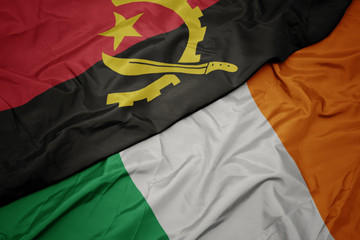 waving colorful flag of ireland and national flag of angola.