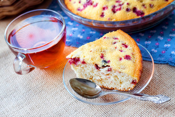 Piece of cowberry pie on glass plate and cup of tea