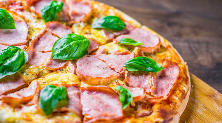 Pizza with Mozzarella cheese, ham, tomato sauce, pepper, Spices and Fresh basil. Italian pizza on wooden table background